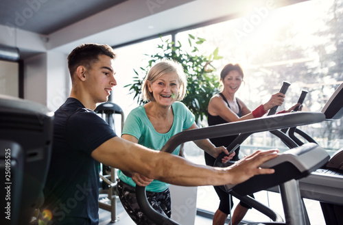 Two cheerful female seniors in gym with a young trainer doing cardio work out.