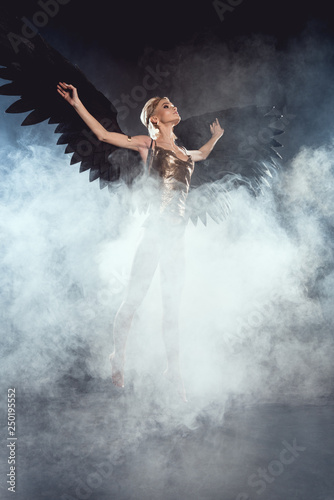 beautiful sexy woman with black angel wings jumping on smoky background
