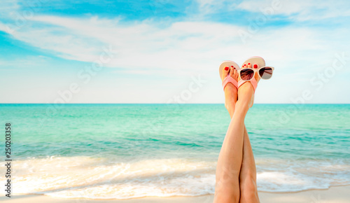 Fototapeta Naklejka Na Ścianę i Meble -  Upside woman feet and red pedicure wear pink sandals, sunglasses at seaside. Funny and happy fashion young woman relax on vacation. Girl on beach. Creative for tour agent. Weekend travel. Summer vibes