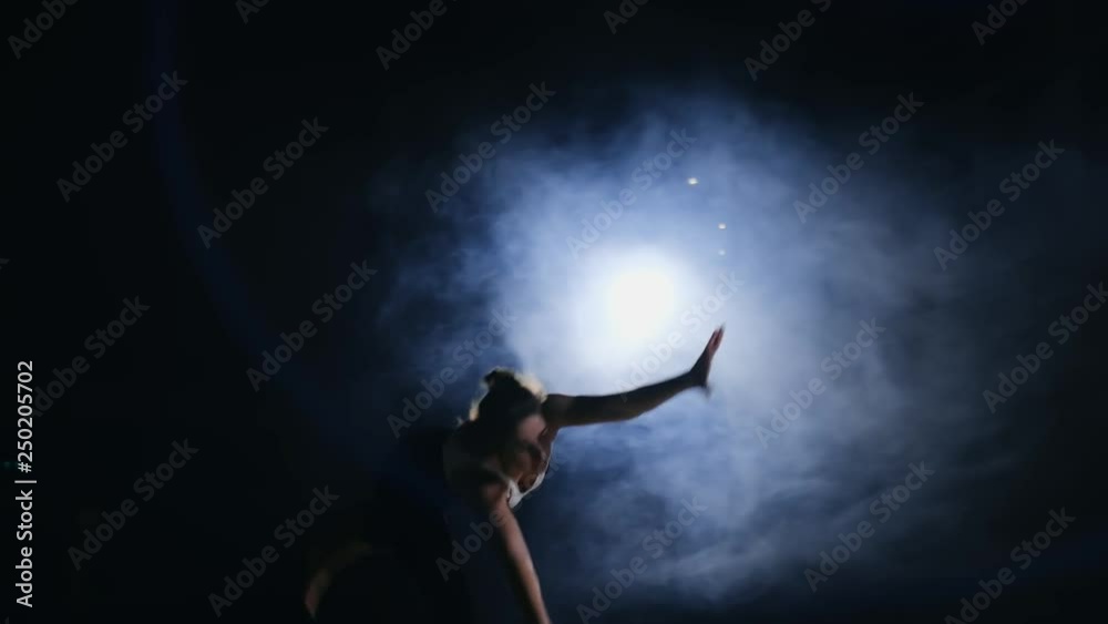 Young female gymnast runs up and performs flips forward and screw in the air in slow motion in gym on carpet in smoke. Young female gymnast runs up and performs flips forward and screw in the air in slow motion in gym on carpet in smoke.