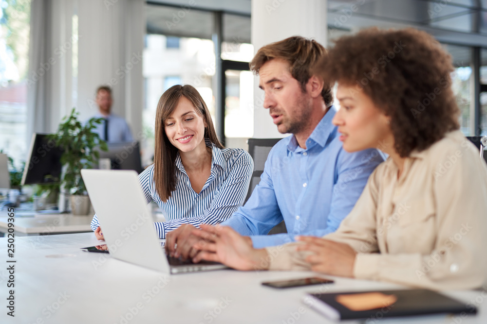Coworkers sitting at table and solving problem. Man using laptop while two female colleagues looking at laptop and helping him.. Coworkers sitting at table and solving problem. Man using laptop while two female colleagues looking at laptop and helping him..