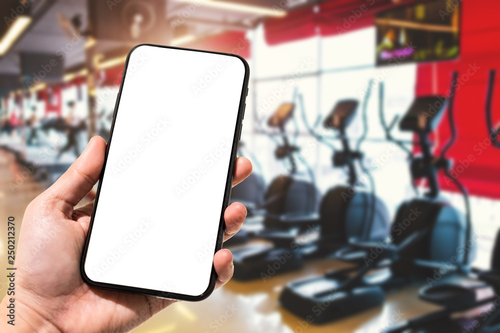 Close-up of female use Hand holding smartphone blurred images touch of Abstract blur of defocused sport gym interior and fitness health club with sports exercise equipment Gym blur background.
