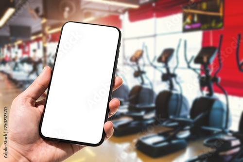 Obraz na płótnie Close-up of female use Hand holding smartphone blurred images touch of Abstract blur of defocused sport gym interior and fitness health club with sports exercise equipment Gym blur background. w salonie