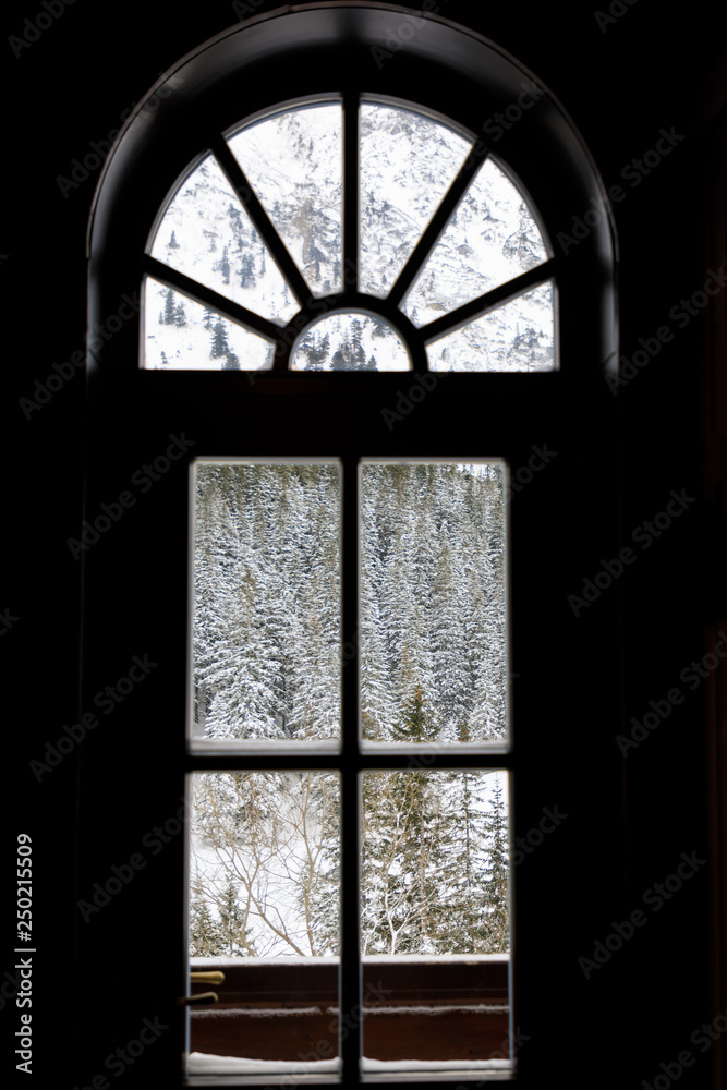 The view of the winter forest in mountains through the wooden window The view of the winter forest in mountains through the wooden window