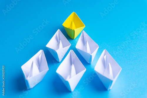 White and yellow paper boat or ship in one direction on blue background. Business for innovative solution concept with selective focus