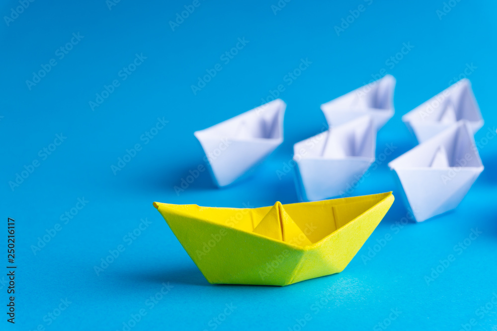 White and yellow paper boat or ship in one direction on blue background. Business for innovative solution concept with selective focus White and yellow paper boat or ship in one direction on blue background. Business for innovative solution concept with selective focus