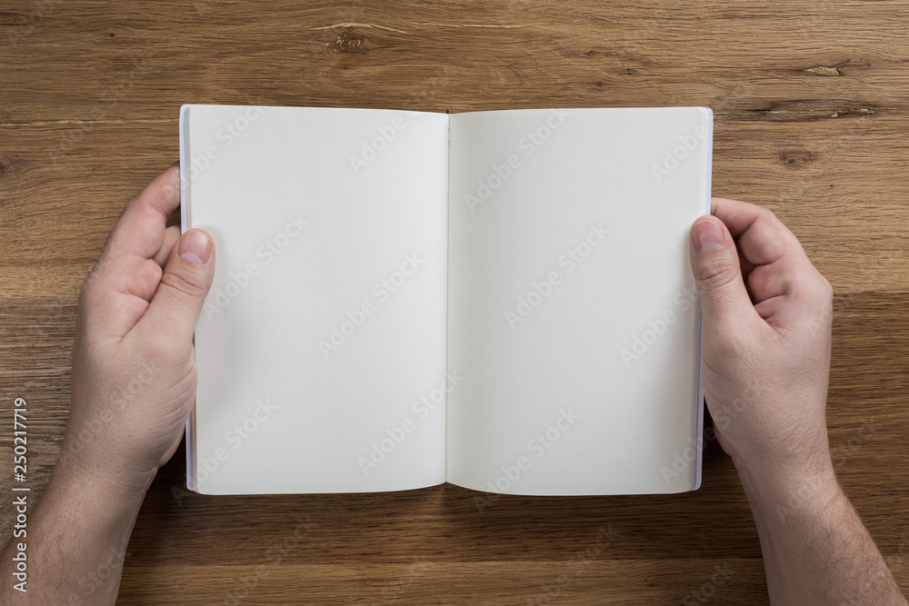 Hand holding white blank paper sheet mockup on wooden background Hand holding white blank paper sheet mockup on wooden background
