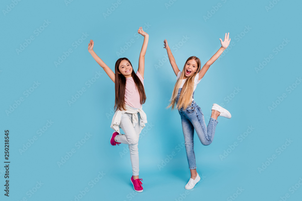 Full length body size view portrait of two people nice attractive cheerful crazy funny funky playful straight-haired pre-teen girls raising hands up chill out rest relax isolated on blue background Full length body size view portrait of two people nice attractive cheerful crazy funny funky playful straight-haired pre-teen girls raising hands up chill out rest relax isolated on blue background