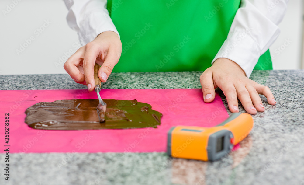 Closeup chocolatier tempering of the chocolate on the marble surface with pyrometer Closeup chocolatier tempering of the chocolate on the marble surface with pyrometer