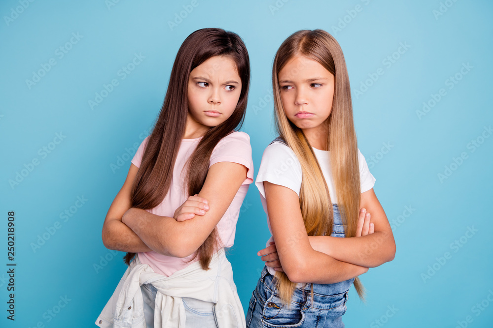 Portrait of two people nice cute lovely attractive sad mad offended gloomy straight-haired pre-teen girls standing back to back folded arms isolated over blue pastel background Portrait of two people nice cute lovely attractive sad mad offended gloomy straight-haired pre-teen girls standing back to back folded arms isolated over blue pastel background