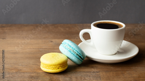 Good morning or Have a nice day message concept - white cup of frothy espresso coffee with colourful French macaroons on dark rustic wooden background