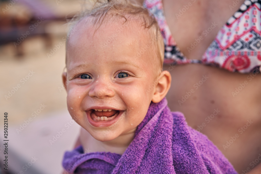 The little boy smiles broadly wrapped in a purple towel after bathing in the sea. The little boy smiles broadly wrapped in a purple towel after bathing in the sea.
