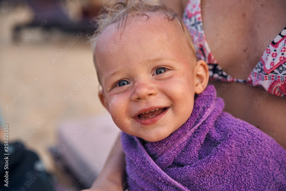 The little boy smiles broadly wrapped in a purple towel after bathing in the sea. The little boy smiles broadly wrapped in a purple towel after bathing in the sea.