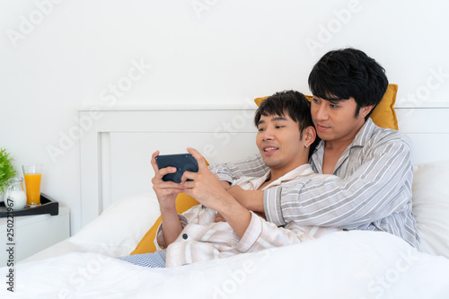Sweet gay couple using mobile and take a selfie in the bed at home