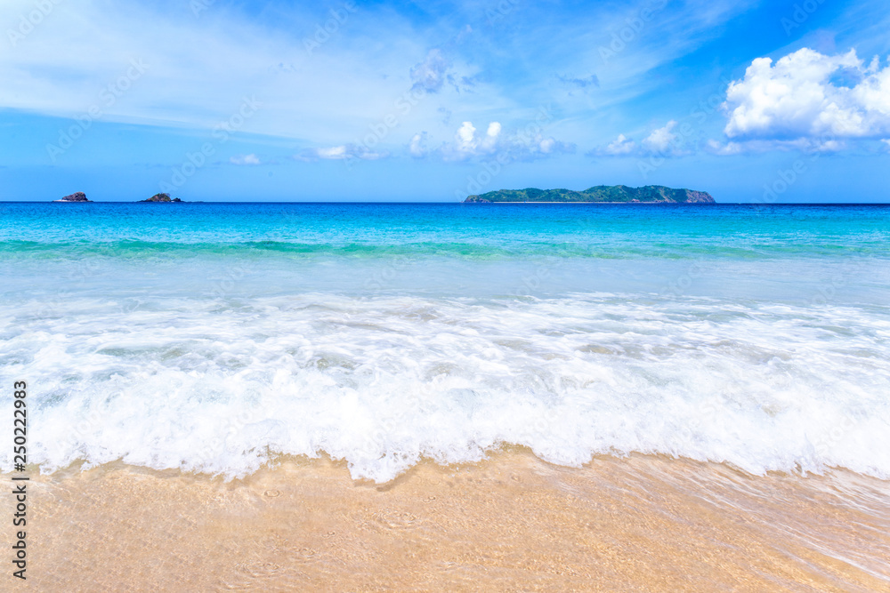 Beautiful amazing gold colored sandy beach with soft waves isolated with sunny blue sky. Concept of tropical calm tourism idea, copy space, close up