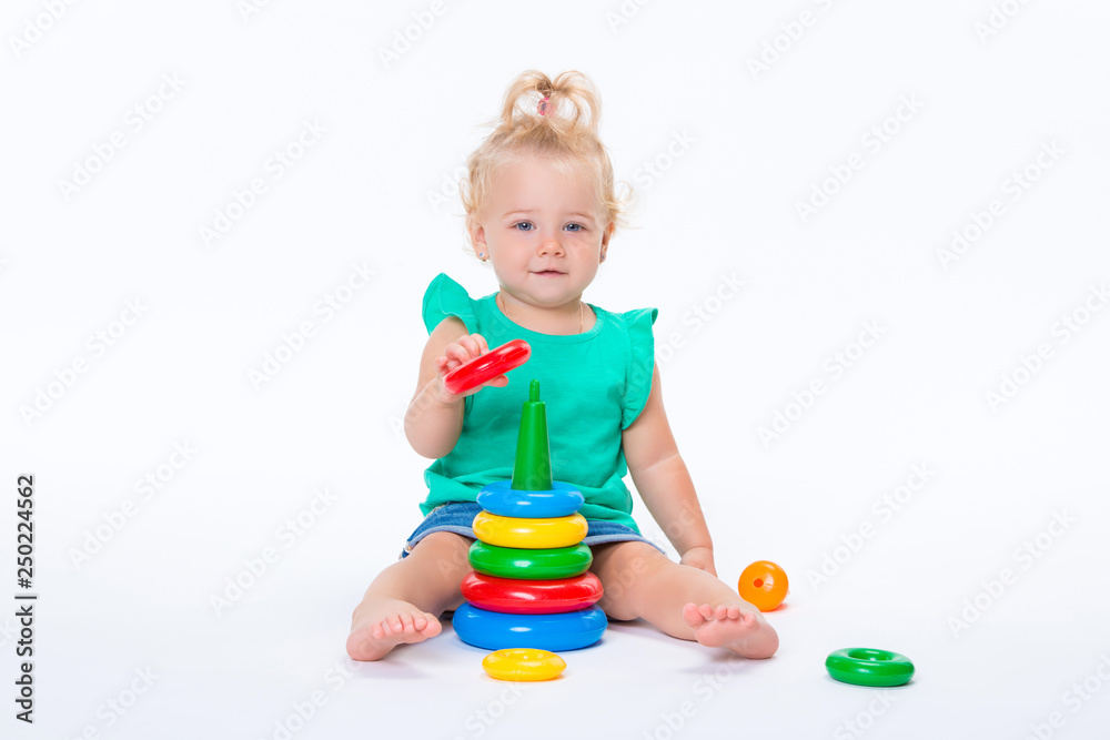Cute kid blonde girl playing with color pyramid toy isolated on white background. Happy childhood and pre-school development of children Cute kid blonde girl playing with color pyramid toy isolated on white background. Happy childhood and pre-school development of children