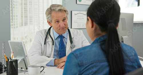 Mature Caucasian male doctor in his office listening to new patient and smiling. Primary care physician going over medical history with Japanese woman