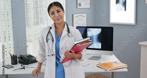 Portrait of Japanese woman doctor standing at her desk looking at camera. Medium shot of confident Asian female physician