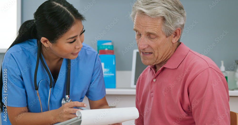 Doctor or nurse talking to senior patient and taking medical history. Older man sitting down in exam room while female physician goes over paperwork with him Doctor or nurse talking to senior patient and taking medical history. Older man sitting down in exam room while female physician goes over paperwork with him