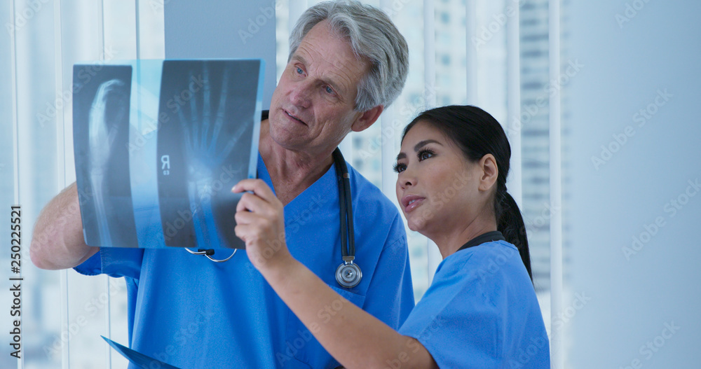 Obraz premium Two medical professionals looking over x-rays of wrist together in hospital. Doctor and nurse looking at broken bones to determine course of care. Senior man and adult woman