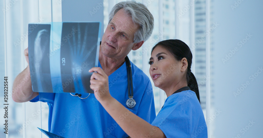 Obraz premium Two medical professionals looking over x-rays of wrist together in hospital. Doctor and nurse looking at broken bones to determine course of care. Senior man and adult woman