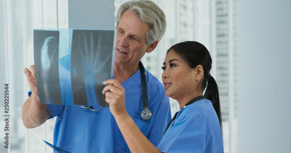 Obraz premium Two doctors looking over x-rays of wrist together in hospital. Medical professionals looking at broken bones to determine course of care. Senior man and adult woman