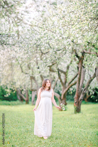 young pregnant girl in white dress walking in the garden