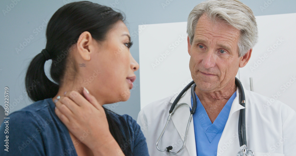 Close up of Senior Caucasian male doctor asking female patient about neck pain in exam room. Medical professional listens to Asian woman explain spinal trouble in hospital Close up of Senior Caucasian male doctor asking female patient about neck pain in exam room. Medical professional listens to Asian woman explain spinal trouble in hospital