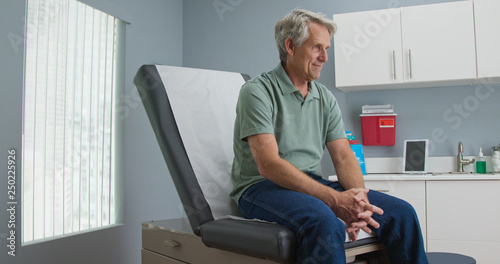 Quadro su tela Senior Caucasian male patient waiting patiently for doctor while sitting on exam room table