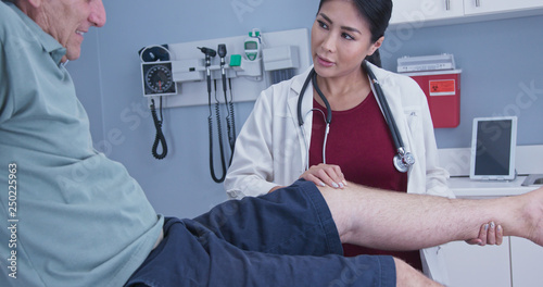 Senior man with hurt knee getting it checked by female medical professional. Physical therapist or doctor with older male patient in exam room checking range of motion on knee injury