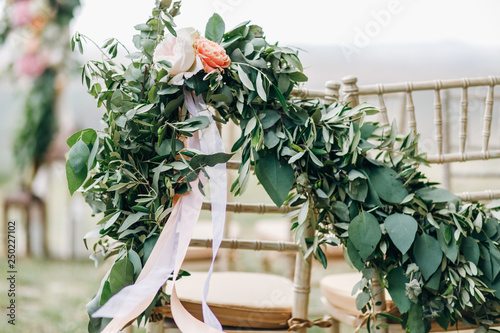 Floral garlands of green eucalyptus and pink flowers decorate wedding arch and chairs on the hill
