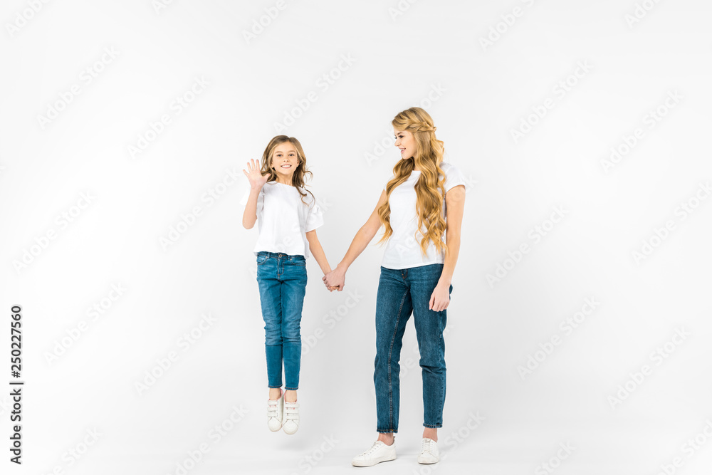 happy daughter jumping and waving hand while holding mothers hand on white background happy daughter jumping and waving hand while holding mothers hand on white background