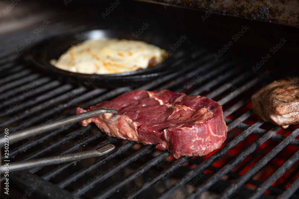 Fresh meat on hot grilled cook with forceps closeup view