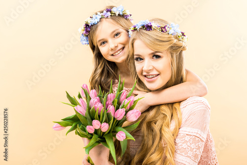 beautiful woman and adorable daughter holding bouquet of pink tulips and looking at camera on yellow background