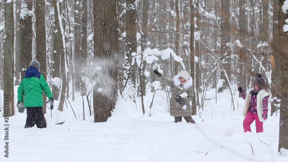 Two little girls playing with a little boy in the snow in winter forest. Throwing snowballs