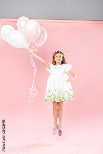 carefree child jumping with white and pink air balloons on bicolor background