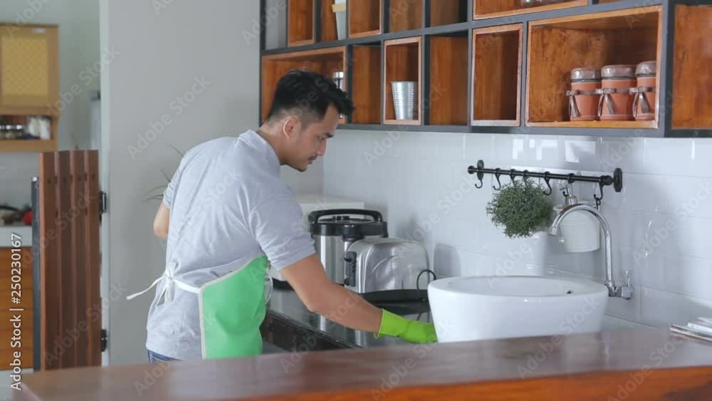 man with apron and rubber gloves wiping wooden table in kitchen