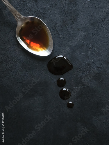 Spoon with leaking soy sauce on the black table.