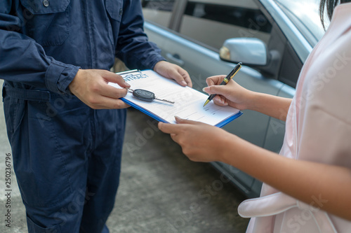 Technicisn repairman giving car key to woman in workshop .Workshop mechanic repair client car in auto service shop. .female customer sign paper insurance bill contact in garage. Fixing car concept.