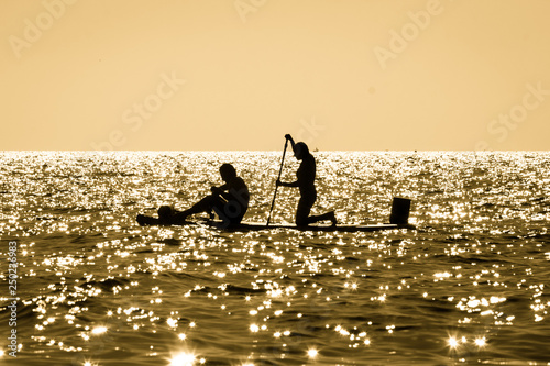 Silhouette of a young couple paddling on a surf at sunset in Maro  Andalusia  Spain.
