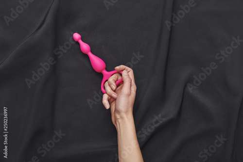 Best anal sex toys. Top view of woman hand holding a pink anal butt plug against of a black silk fabric