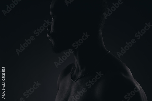 Dark key profile portrait of young muscular shirtless male model with neck chain.
