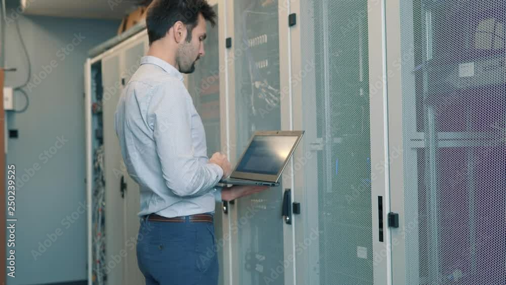 Server IT Engineer In Data Center Server Room.Network Engineer Working Laptop Computer.Server Rack Room Works.Programmer Checks A work Of Server At A Data Center. Server IT Engineer In Data Center Server Room.Network Engineer Working Laptop Computer.Server Rack Room Works.Programmer Checks A work Of Server At A Data Center.