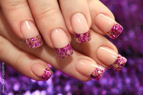 Brilliant French manicure with lilac and golden small glitters on a purple background close-up. File art.