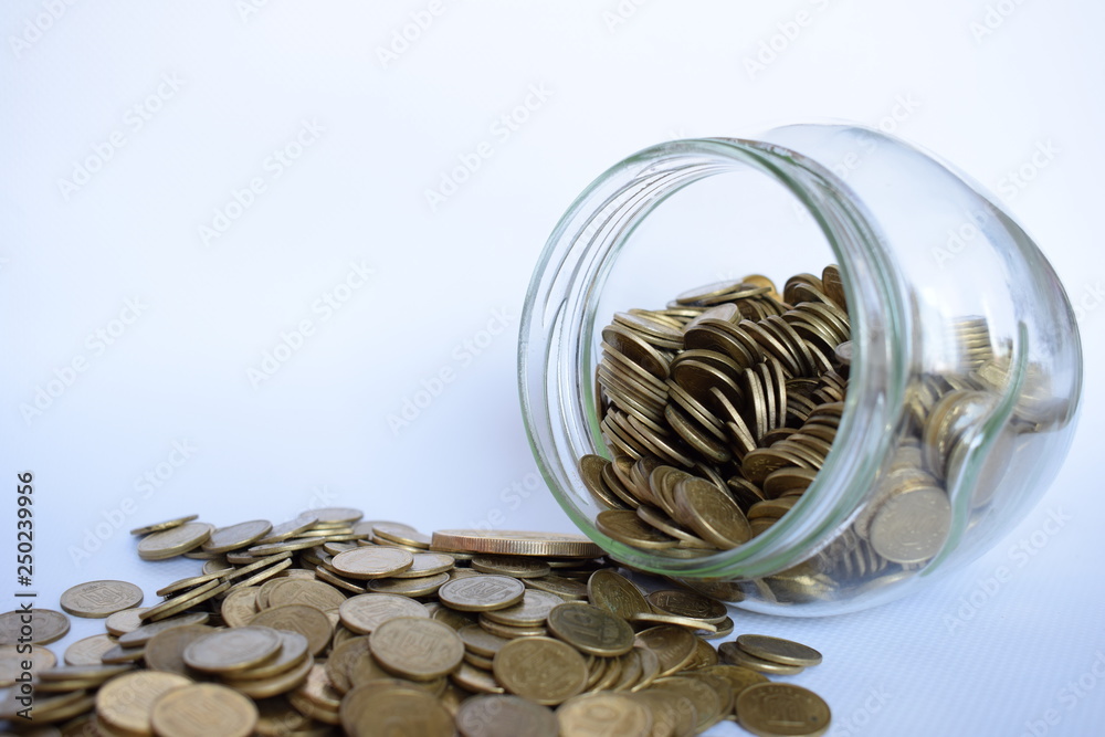 Close up coins in glass jar on white table. Coins scattered around. Isolated on white background. Saving concept Close up coins in glass jar on white table. Coins scattered around. Isolated on white background. Saving concept