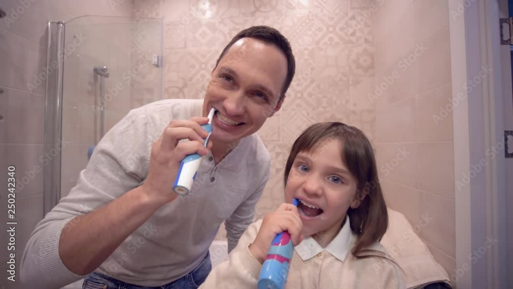 oral hygiene, joyful dad with daughter with toothbrush brushing teeth in front of mirror at washroom oral hygiene, joyful dad with daughter with toothbrush brushing teeth in front of mirror at washroom