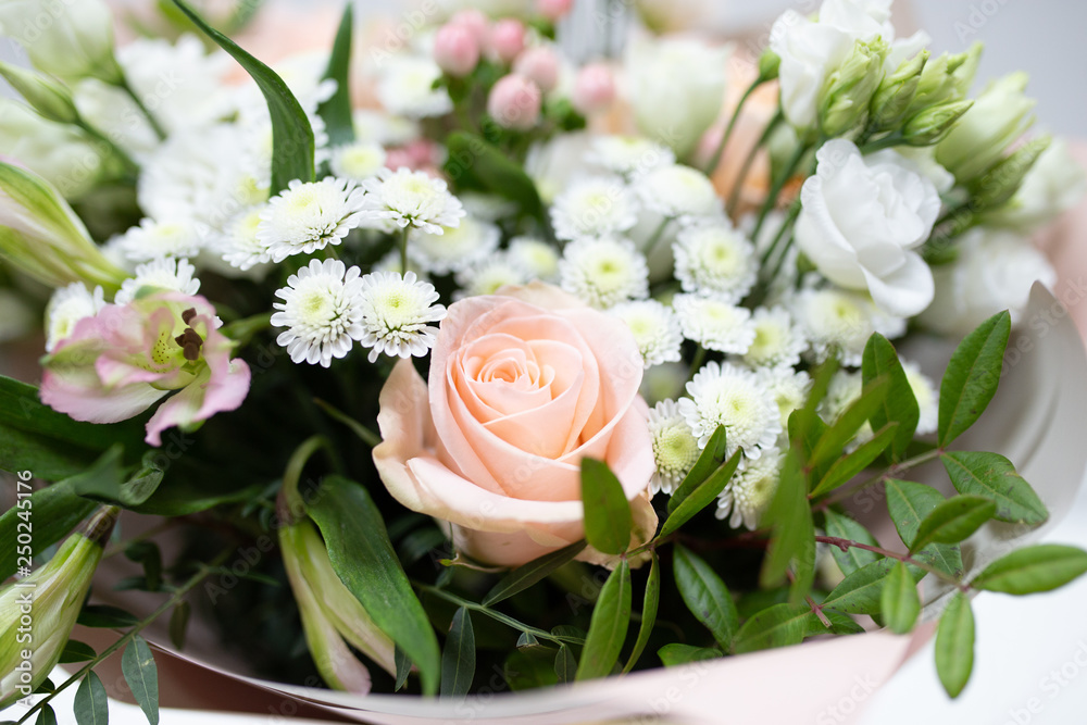 Delicate bouquet of fresh flowers (Main colors: white and pink) in a paper packaging in a vase on a light background.