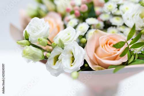 Delicate bouquet of fresh flowers (Main colors: white and pink) in a paper packaging in a vase on a light background.