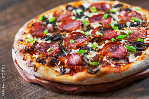 Pizza with Mozzarella cheese, salami, pepper, pepperoni, olives, Spices and mushroom. Italian pizza on wooden table background