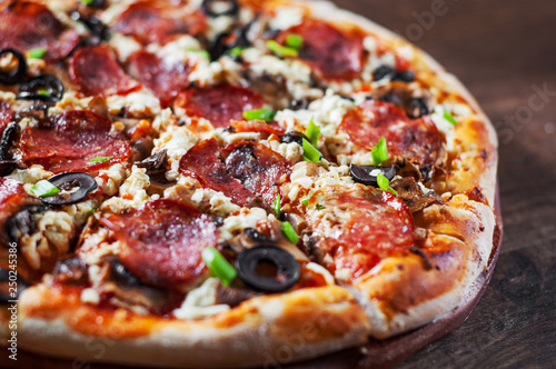 Pizza with Mozzarella cheese, salami, pepper, pepperoni, olives, Spices and mushroom. Italian pizza on wooden table background
